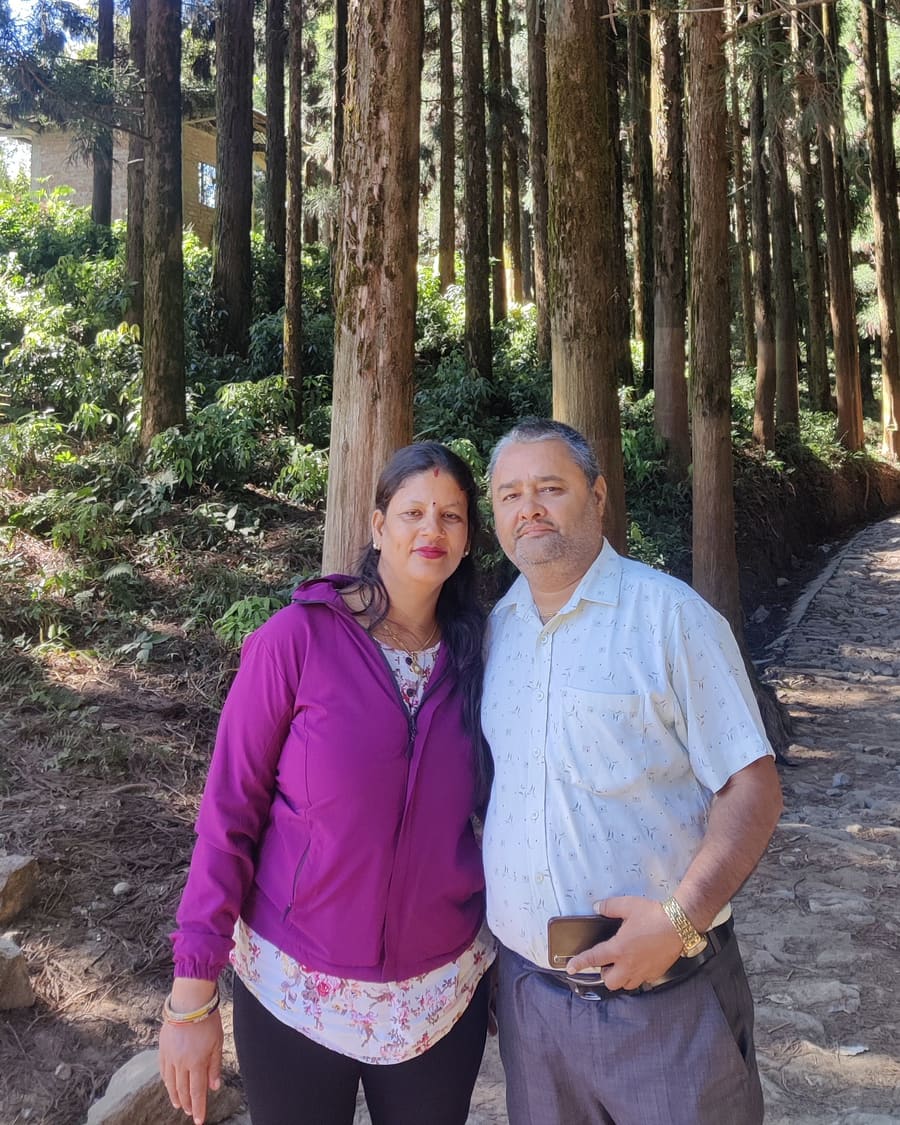 Devi Lal Subedi and Ambika Subedi standing together on a tree-lined path
